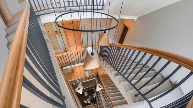 A spiral staircase with wooden handrails and black metal railings, leading to a lower level with a circular ceiling light fixture.