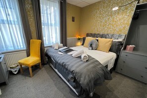 A hotel room with a bed, a chair, a dresser, and a window with curtains.