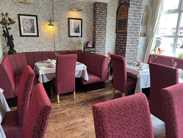A restaurant interior with red patterned booths, white tables, framed pictures on the wall, and a menu board.
