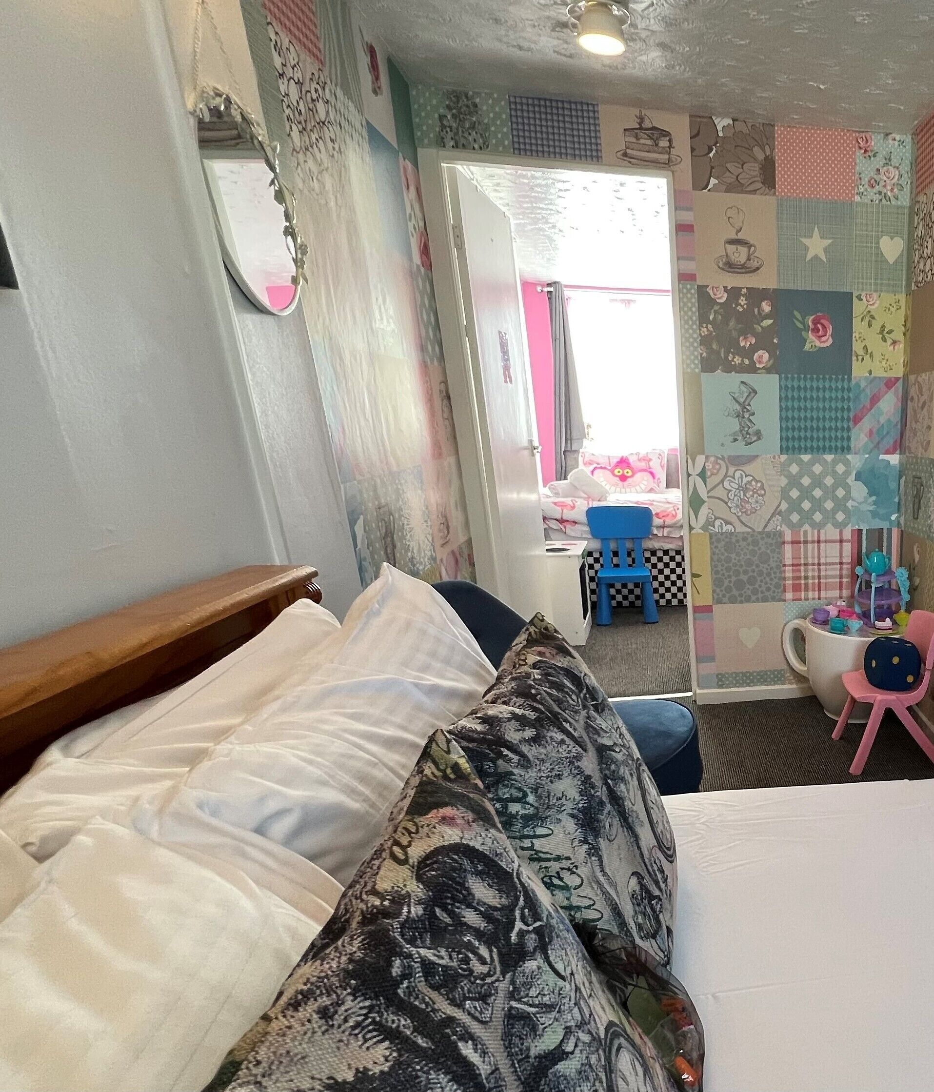 A bedroom with a bed, a mirror, and a colorful patchwork wall.