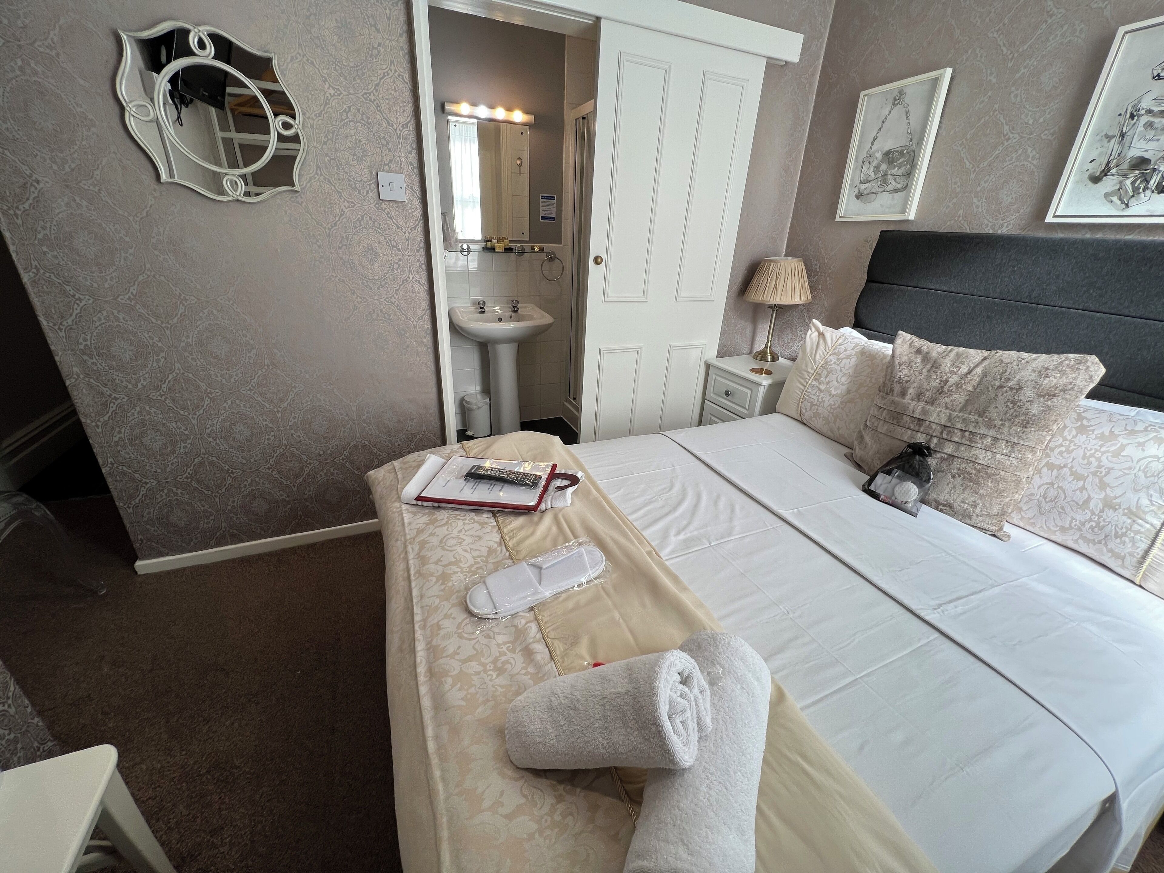 A hotel room with a bed, a bedside table, a mirror, a sink, and a lamp.