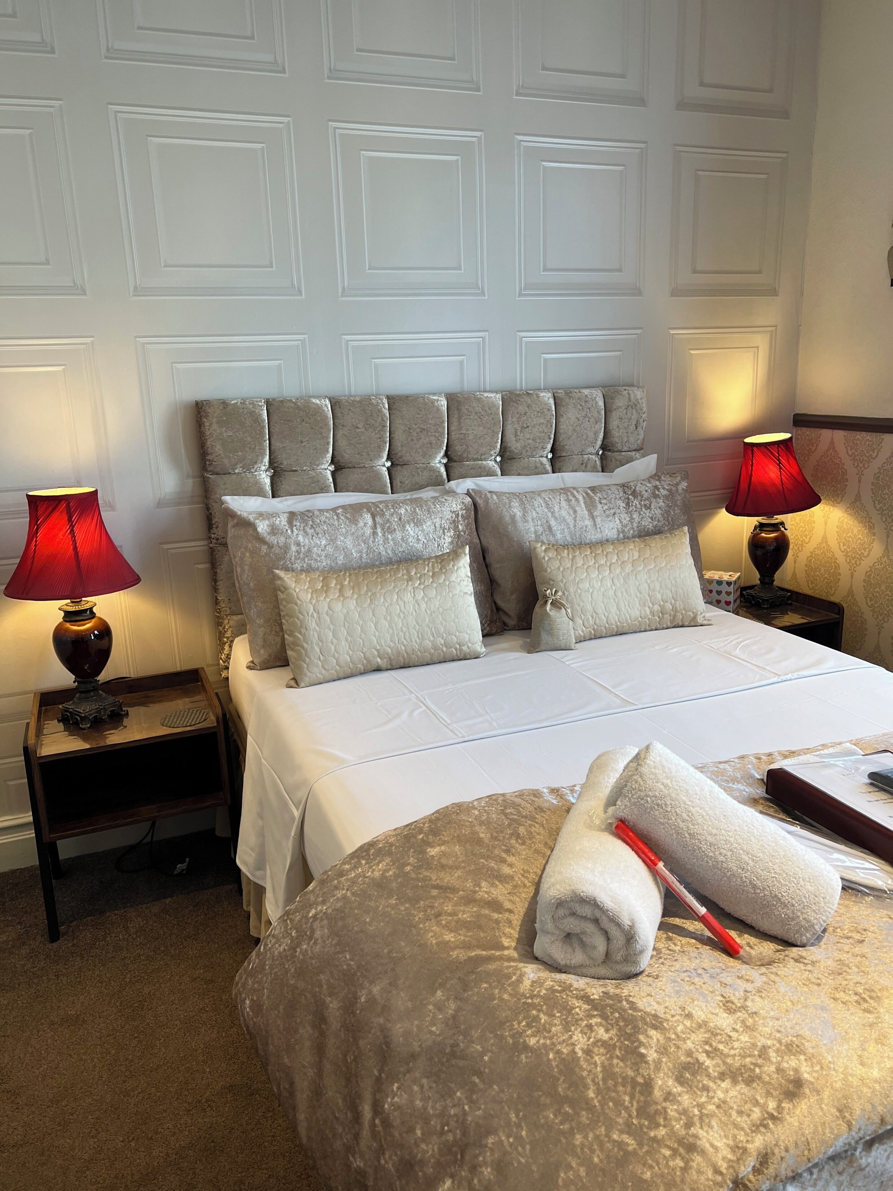 A neatly made bed with a headboard, two bedside tables with lamps, and a rolled towel on the bed.