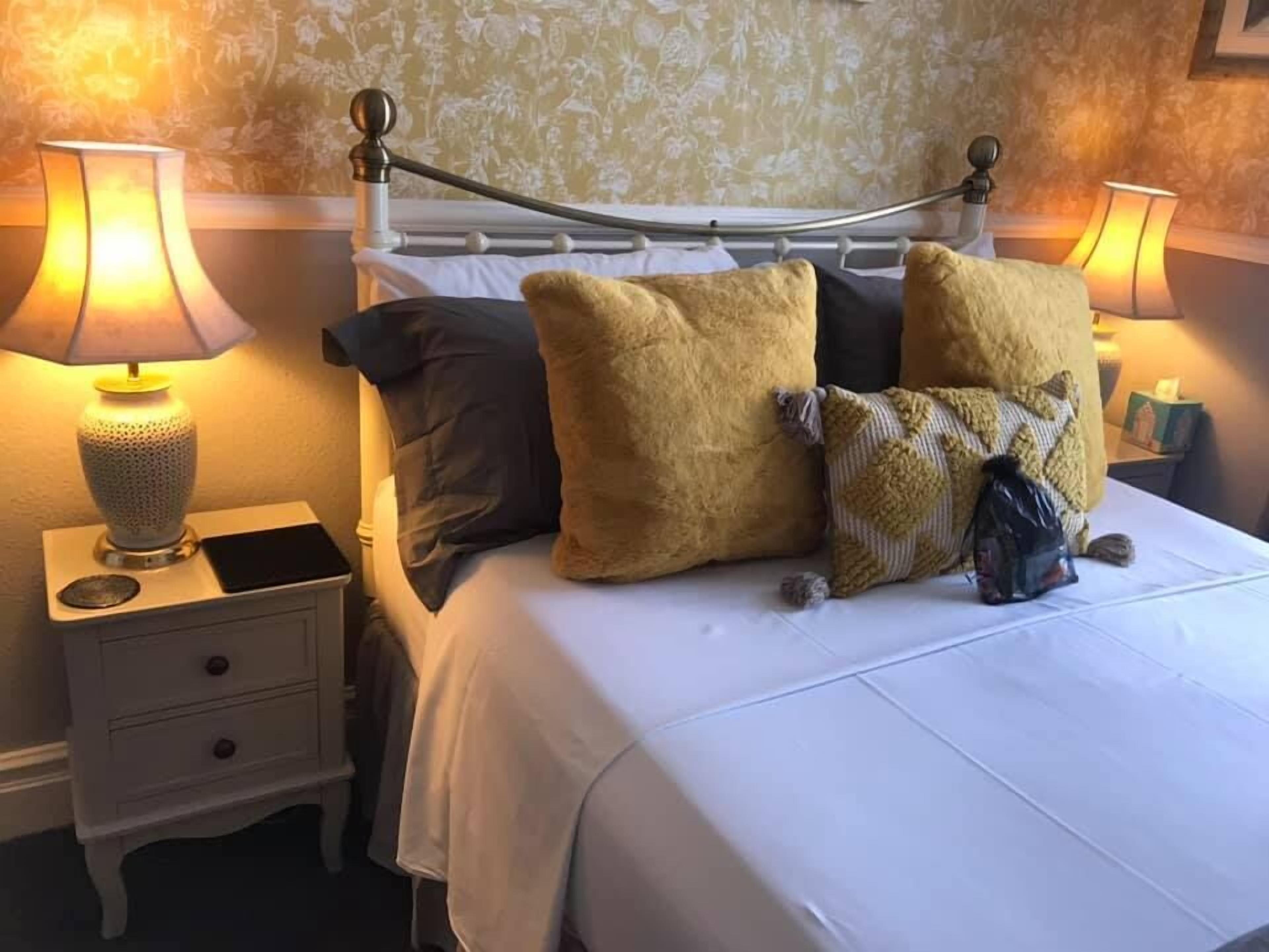 A neatly made bed with a white comforter and multiple pillows, two bedside lamps, and a small bedside table with a lamp.