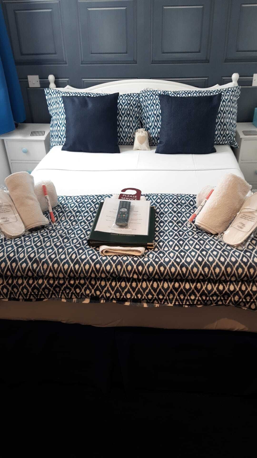 Un lit bien fait, avec une literie à motifs, une télécommande, un livre et des articles de toilette.