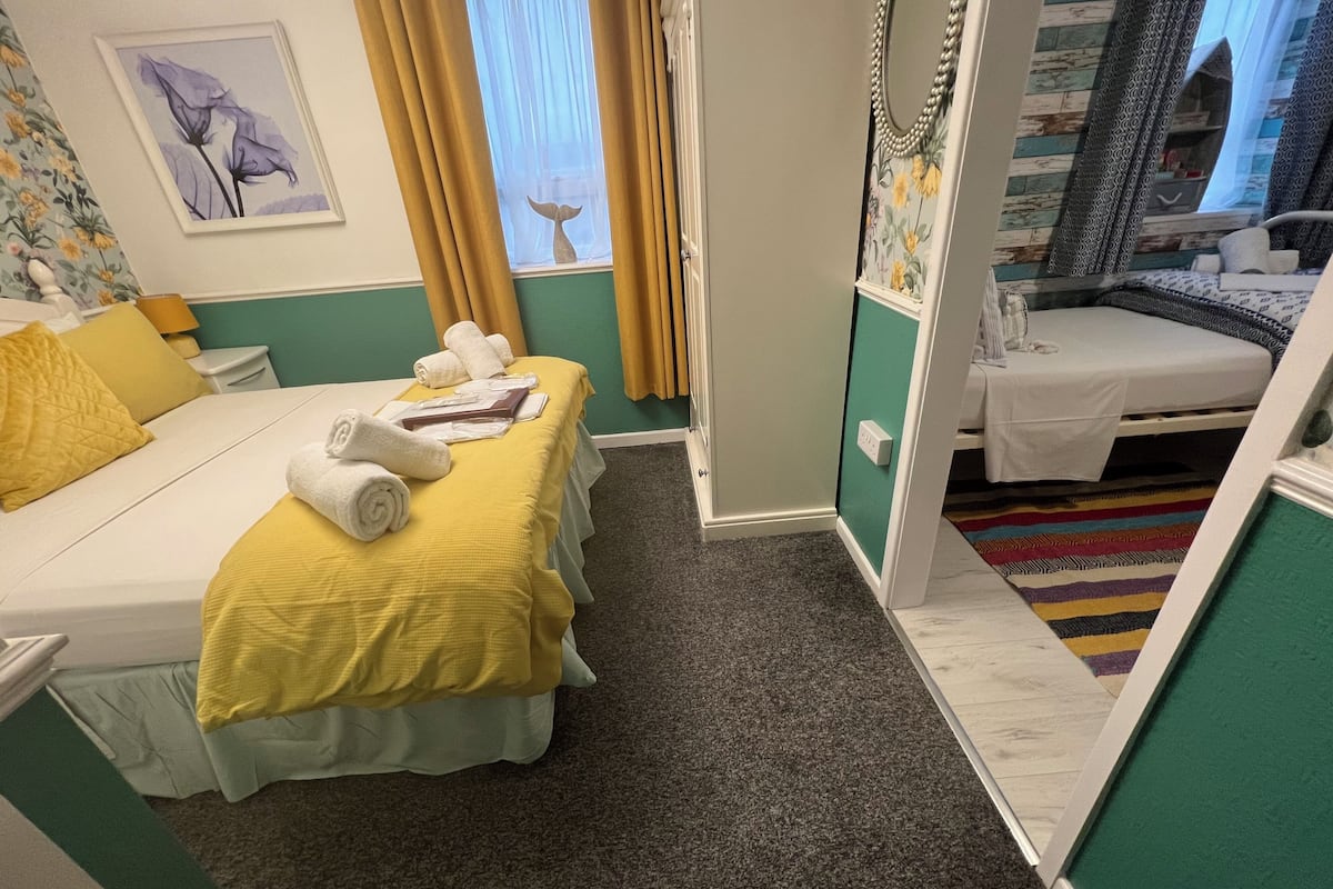 Habitación de hotel con cama, una mesita con toallas, un espejo y una ventana con cortinas.