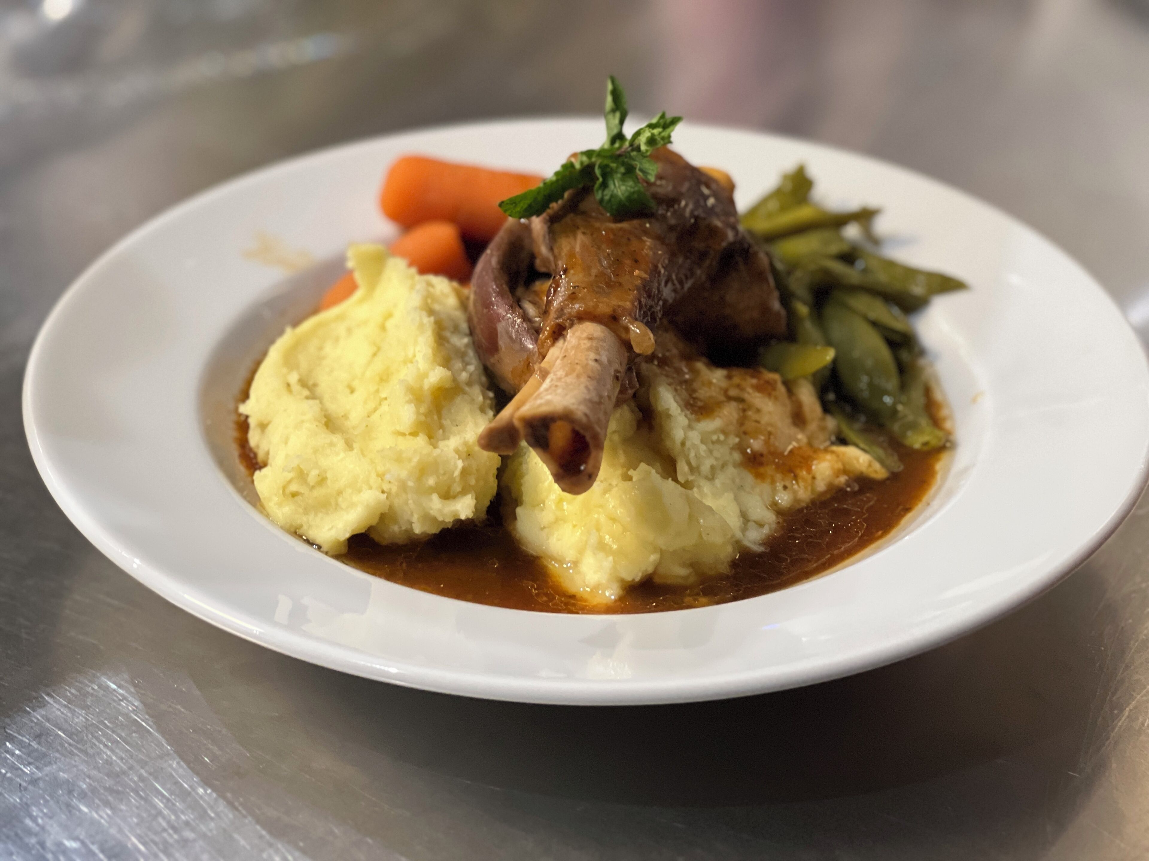A plate of food with mashed potatoes, a piece of meat, carrots, and green beans.