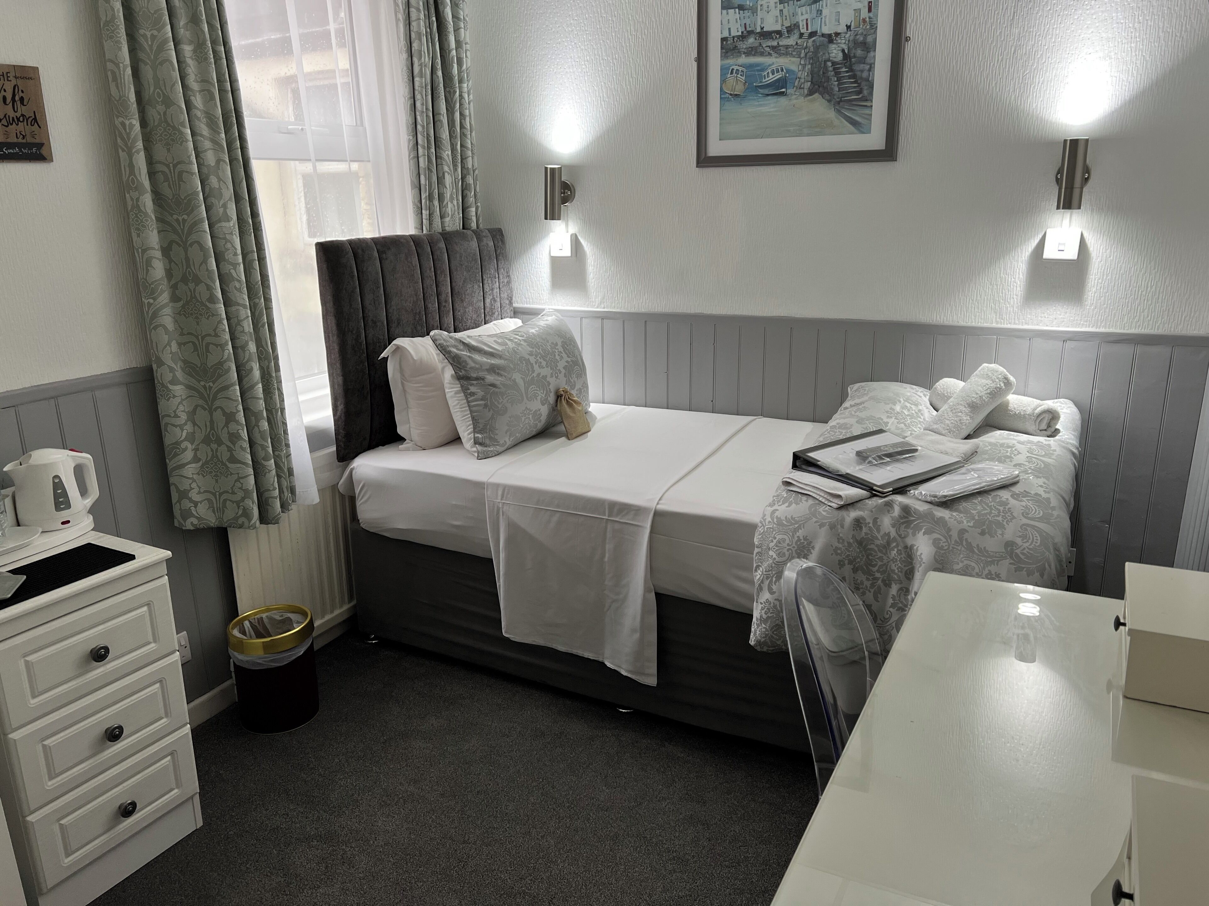 Une chambre d’hôtel avec un lit, des tables de chevet, une bouilloire, une poubelle et un tableau au mur.