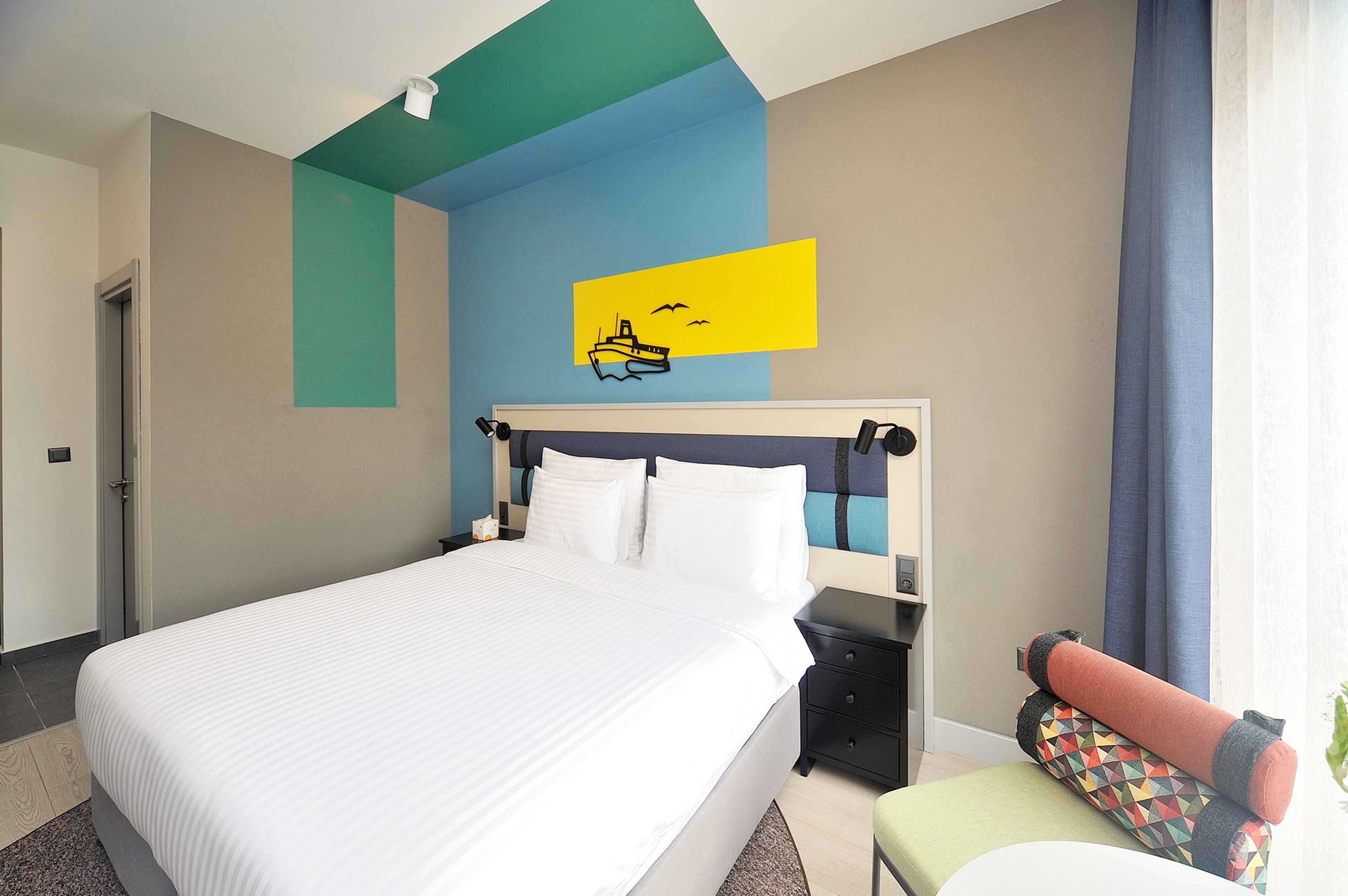 Una habitación de hotel con una cama, una mesita de noche, una silla y una pared con diseño azul y amarillo.