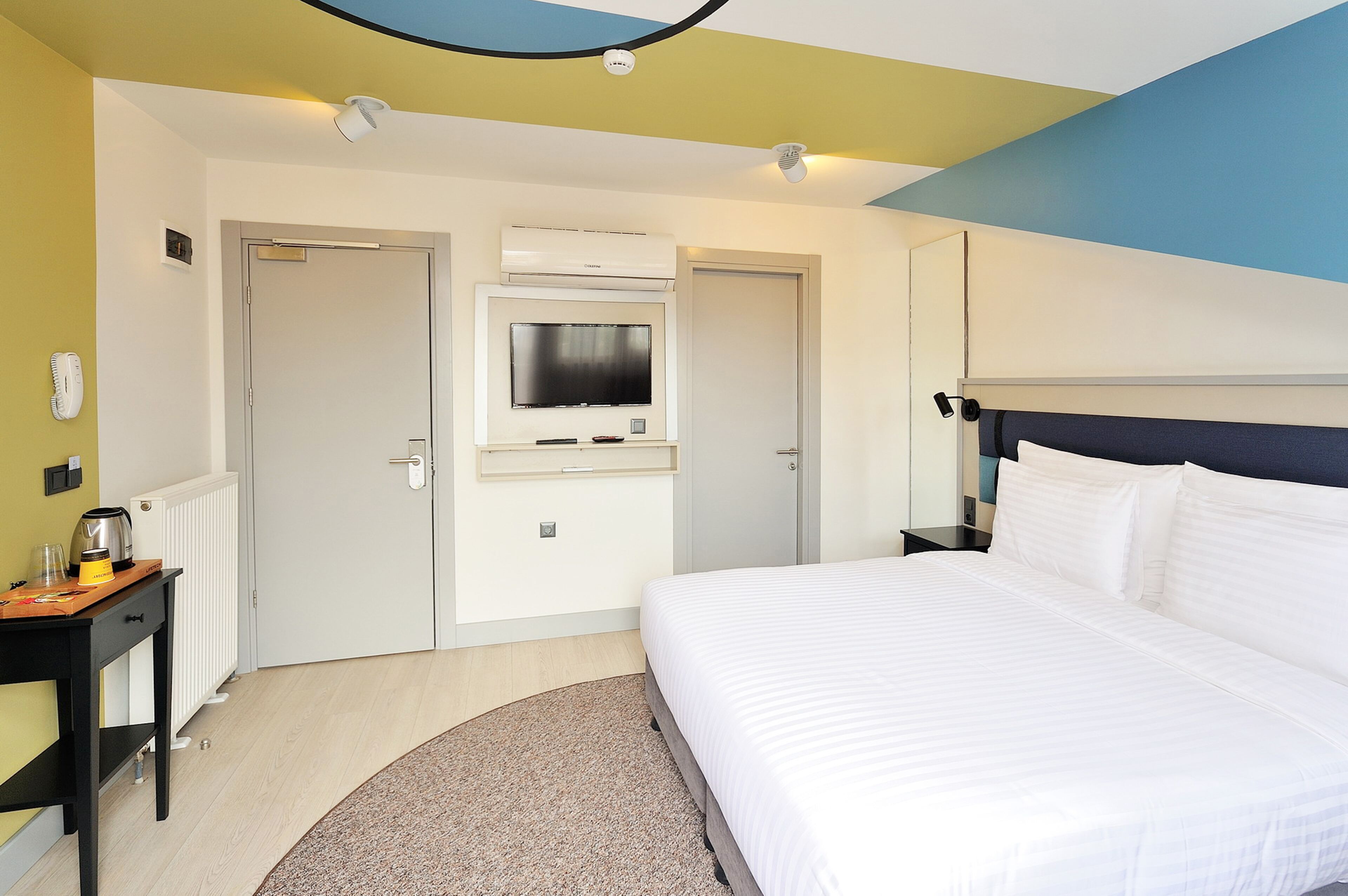 A hotel room with a bed, a desk, a chair, a television, and a radiator.