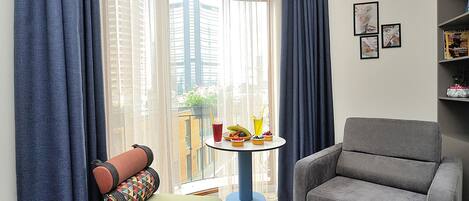 Un salon moderne avec un canapé, un fauteuil et une petite table sur laquelle se trouvent une boisson et des fruits.