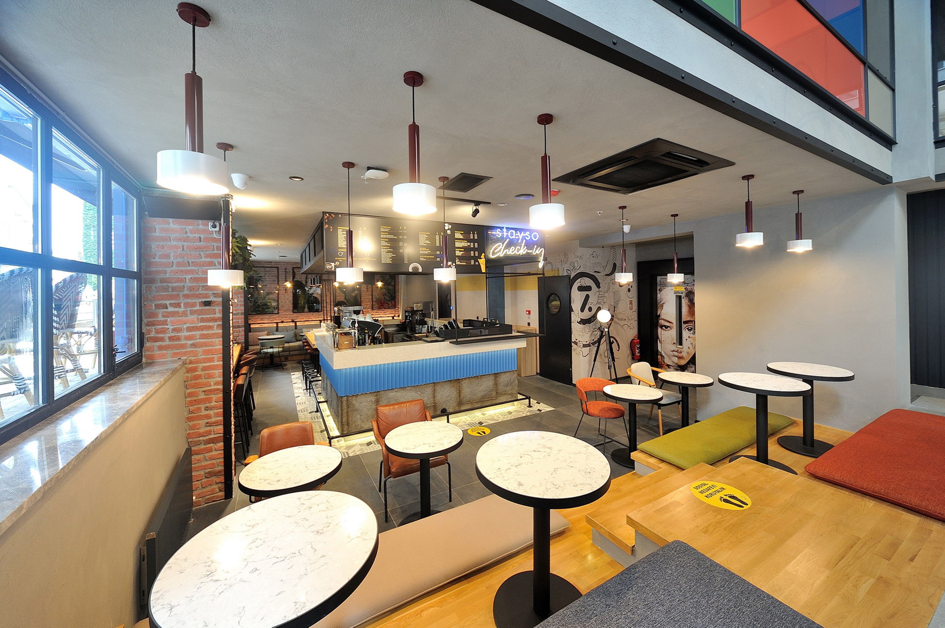 Un café moderno con zona de bar, diversas opciones de asientos, incluyendo mesas redondas y bancos, además de un cartel de menú visible.
