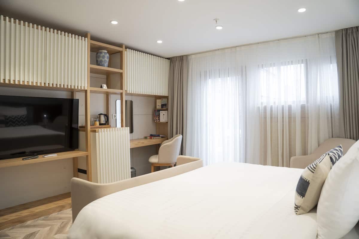 A modern hotel room with a large bed, a TV, a desk, and a chair.