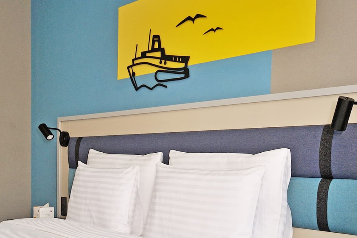 A neatly made bed with white linens, a headboard with a striped pattern, and a nightstand with a lamp.