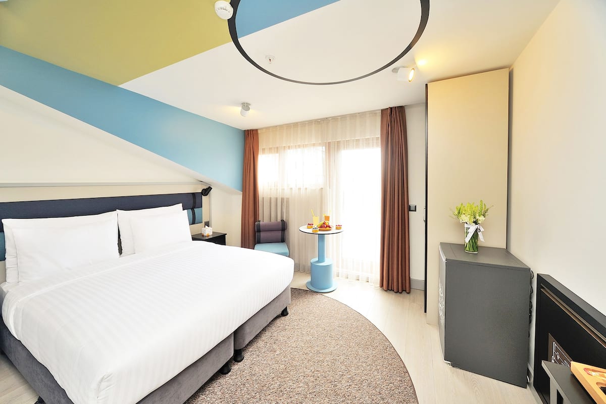 A hotel room with a large bed, a small table with a vase, and a fireplace.