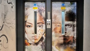 Dos puertas de ascensor con murales artísticos y señales de límite de peso.