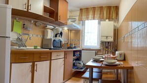 Cozinha compacta com geladeira, micro-ondas e fogão. Armários de madeira e janela com cortinas.