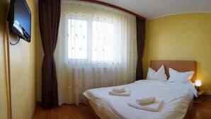 Quarto de hotel com cama, televisão na parede, janela com cortinas e abajur.