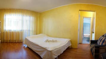 A bedroom with a bed, a chair, a shelf, and a door leading to another room.