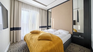 A hotel room with a bed, curtains, a mirror, and a patterned floor.