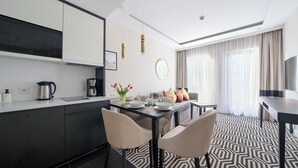 A modern hotel room with a kitchen area, dining table, and seating.