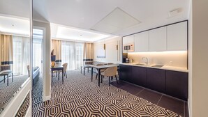A modern hotel room with a dining area, a kitchen with a microwave, and a patterned floor.