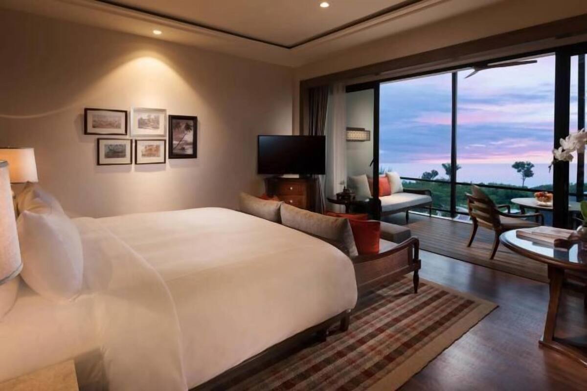 A hotel room with a large bed, a TV, a dining area with a table and chairs, and a balcony with a view.