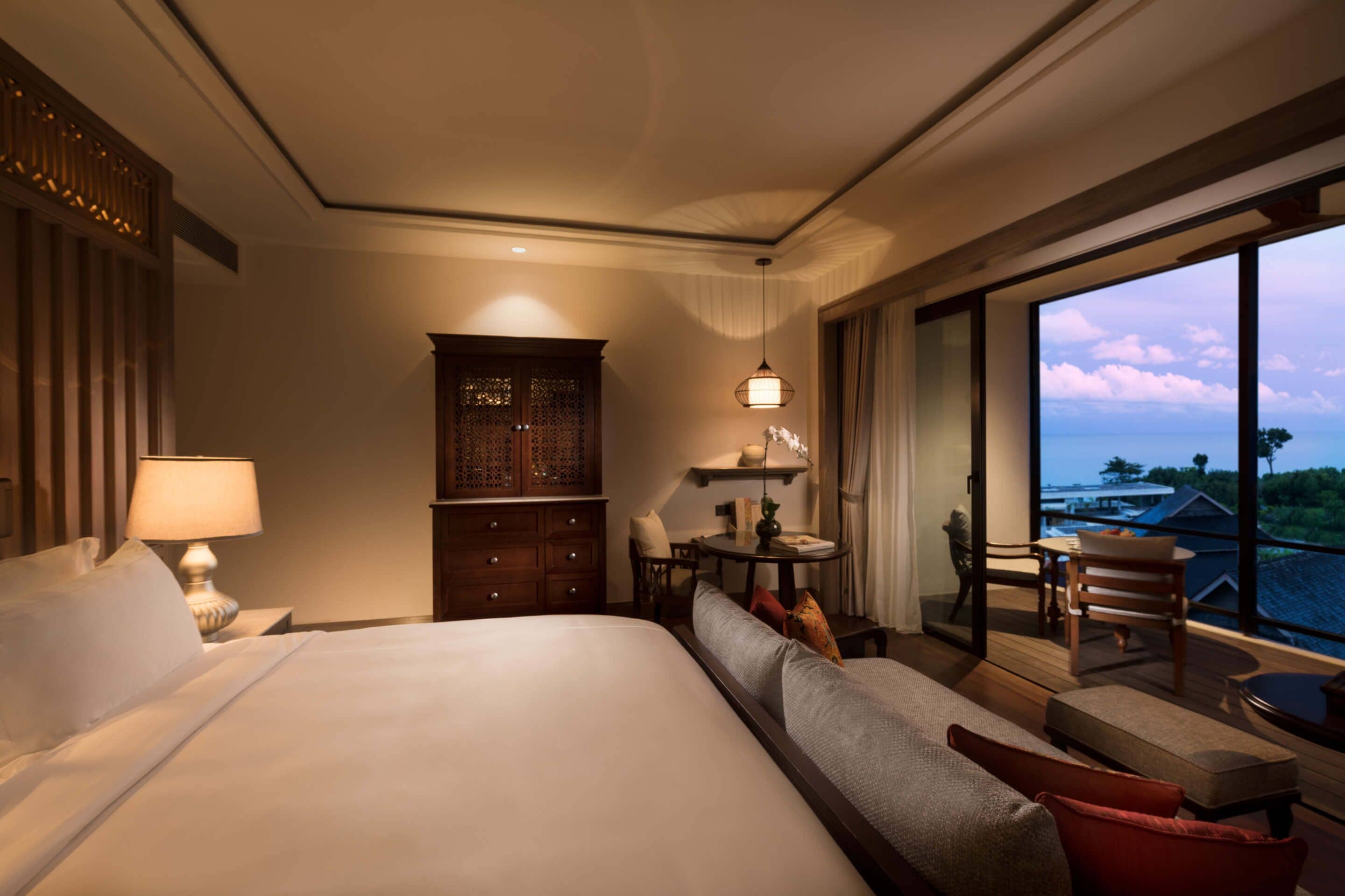 A hotel room with a large bed, a desk, a chair, a sofa, and a view of the ocean.