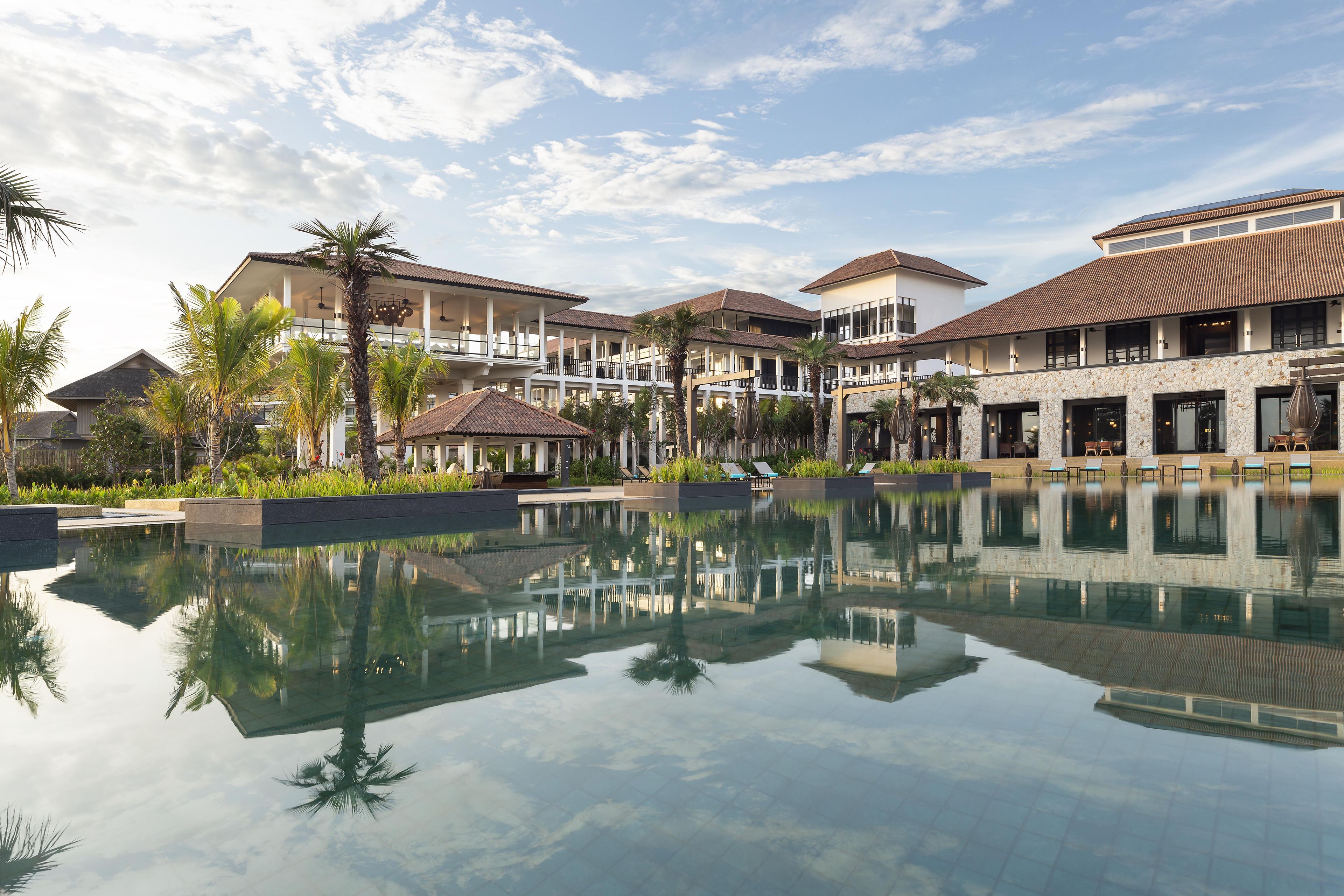 A resort with a large pool, multiple buildings, and palm trees.