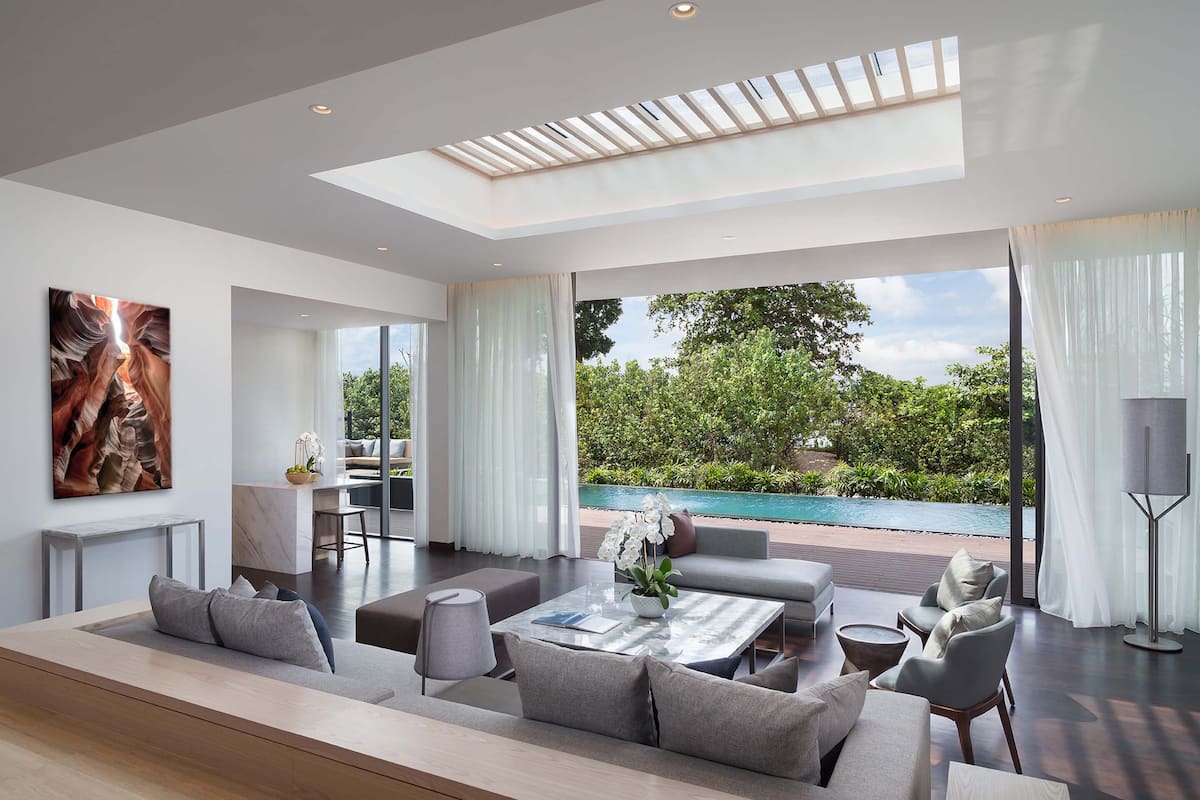 A spacious living area with a large window overlooking a pool, a modern sofa set, and a dining area with a table and chairs.