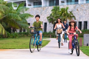 A pathway with people riding bicycles, surrounded by greenery and a building with a stone facade. - Anantara Desaru Coast Resort & Villas (Bandar Penawar)