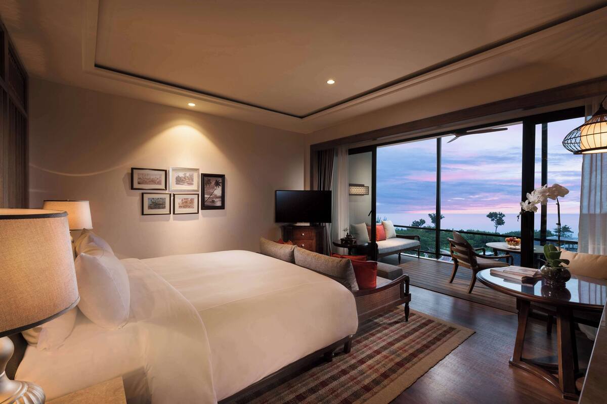 A hotel room with a large bed, a TV, a desk with a chair, and a balcony with a view.