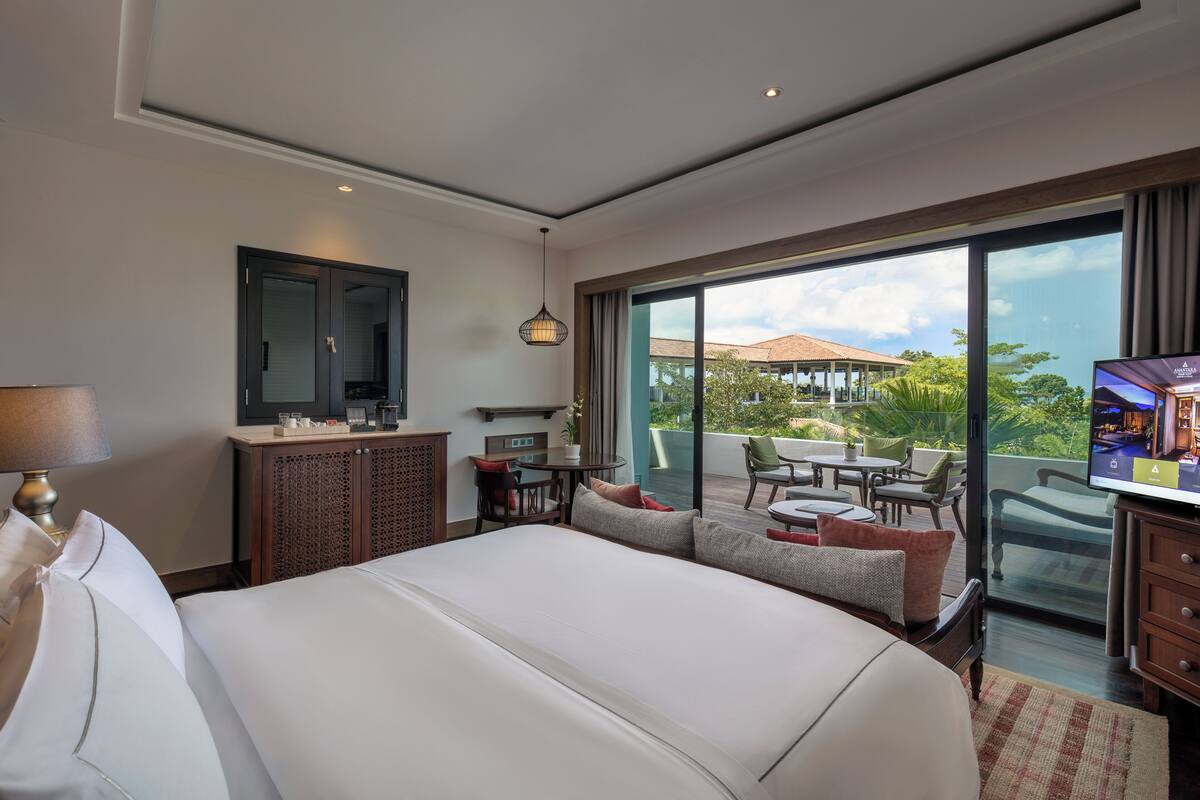 A hotel room with a large bed, a TV, a desk, and a balcony with outdoor seating.