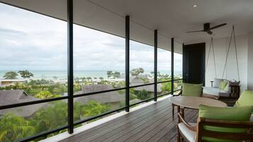 Ein Balkon mit Blick auf das Meer und Häuser, Holzmöbel und ein Deckenventilator.