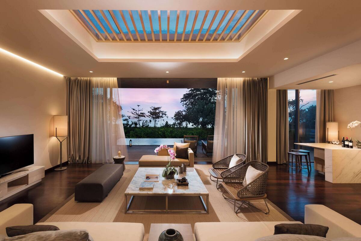 A modern living room with a large flat-screen TV, comfortable seating, a coffee table, and a view of the outdoors.