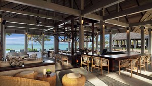 A spacious outdoor bar area with wicker furniture, a central bar, and a view of the sea.