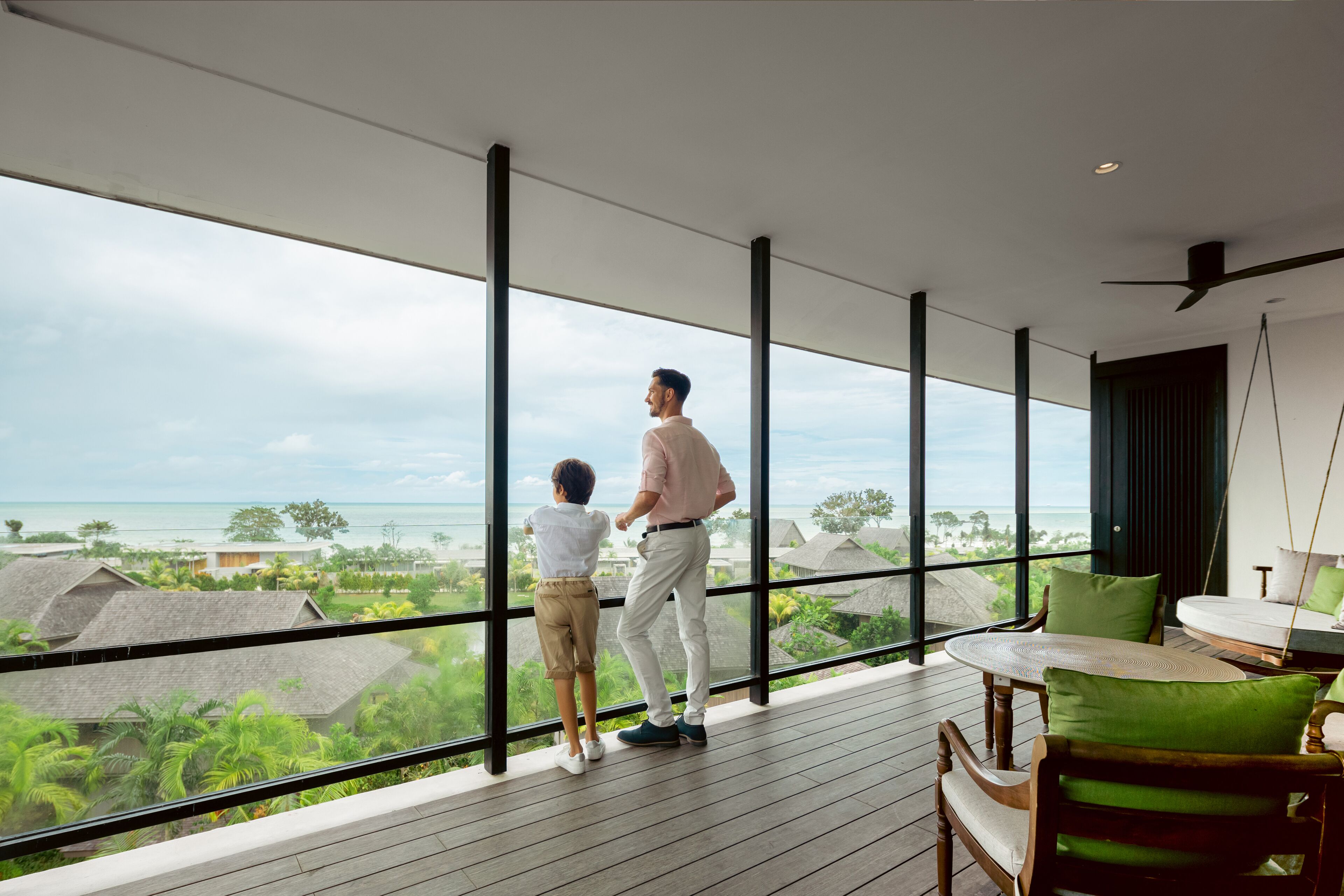 Une chambre moderne dotée de grandes fenêtres donnant sur un paysage tropical et l’océan.