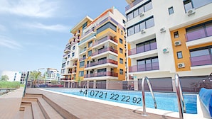 A multi-story residential building with balconies, a swimming pool, and a wooden deck area. - Apart holiday Coralia Mamaia CityLiving (Constanta)