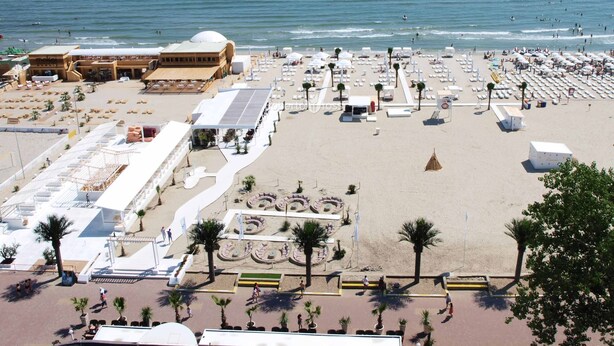 A beach with a large open area, a building with a dome, and a pier extending into the sea. - Apart holiday Coralia Mamaia CityLiving (Constanta)