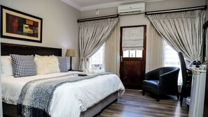 A hotel room with a large bed, a chair, a desk, and a window with curtains. - Uitzicht Guest house (Kimberley)