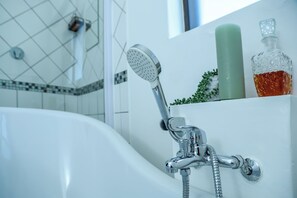 A bathroom with a white bathtub, a handheld showerhead, a green bottle, and a decorative glass bottle. - Uitzicht Guest house (Kimberley)
