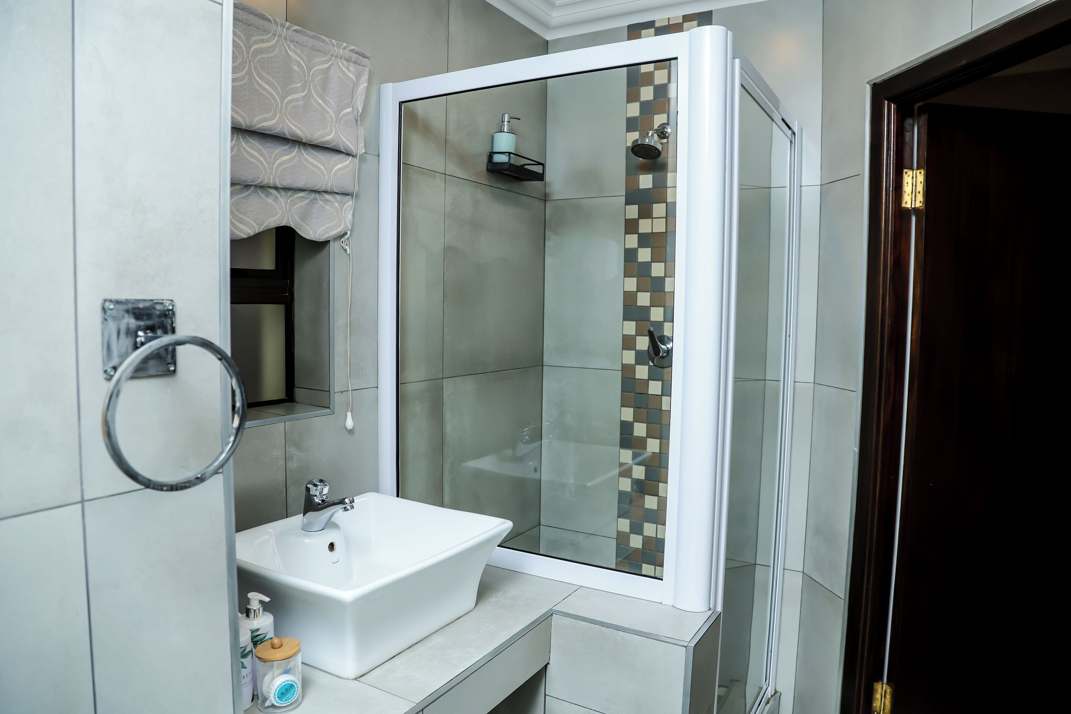 Een moderne badkamer met een douchecabine van glas, een witte wastafel en een handdoekhouder.