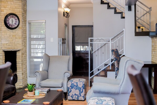 A modern living room with a fireplace, a staircase, and a clock on the wall. - Uitzicht Guest house (Kimberley)