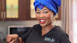 A person holding a plate with food, wearing a black shirt with a logo, and a blue headscarf. - Uitzicht Guest house (Kimberley)