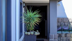 A modern building with a sloped roof, a large planter with plants, and a paved entrance area. - Uitzicht Guest house (Kimberley)