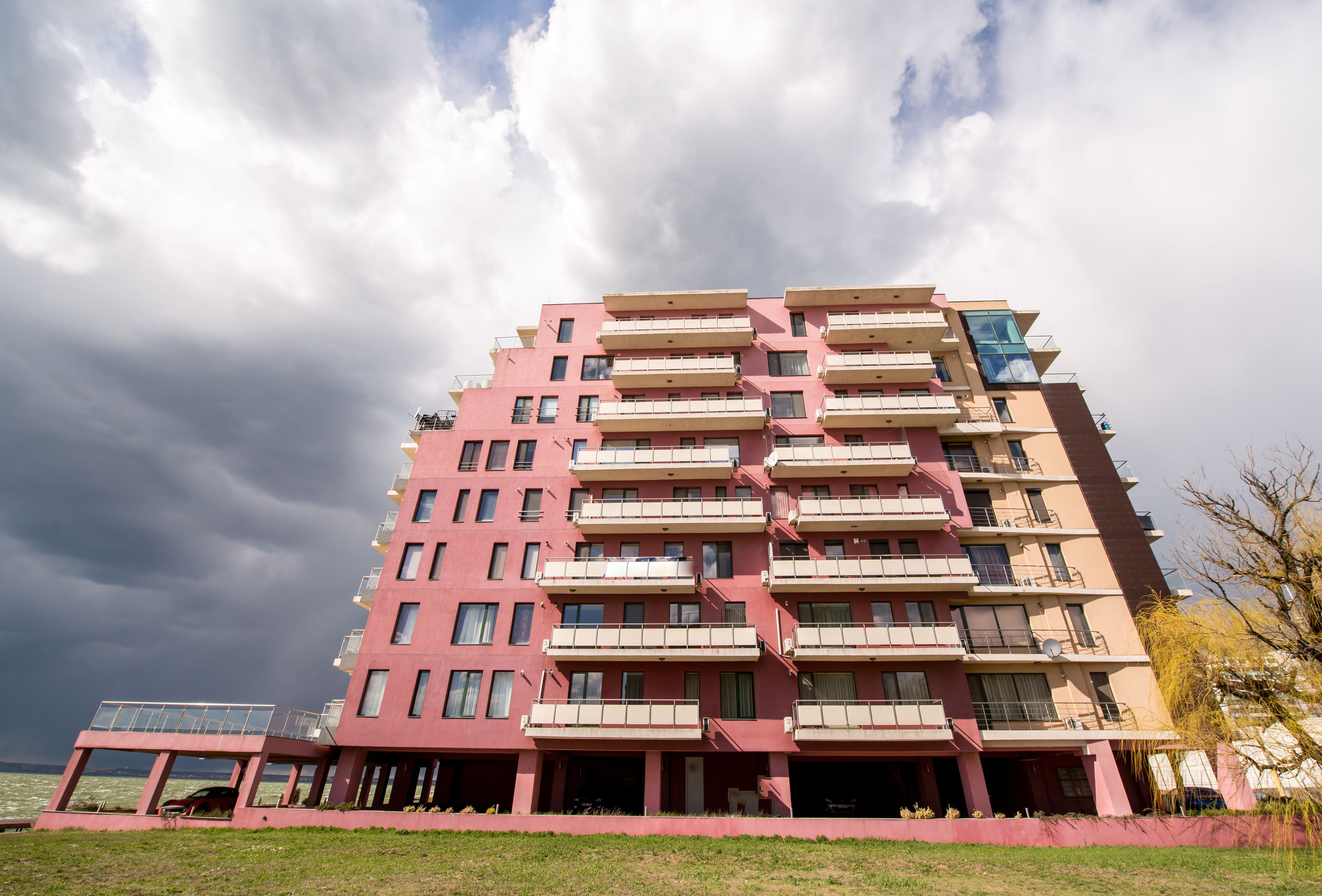 A multi-story residential building with balconies, a flat roof, and a view of the sea.
