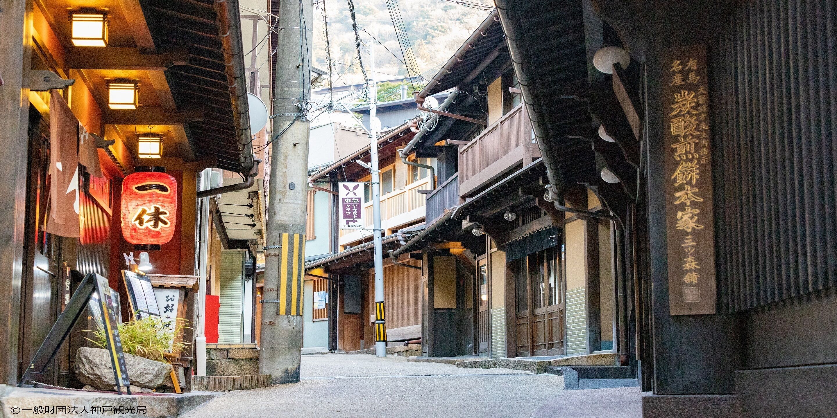 A narrow street with traditional Japanese architecture, including wooden buildings with tiled roofs and signage in Japanese.