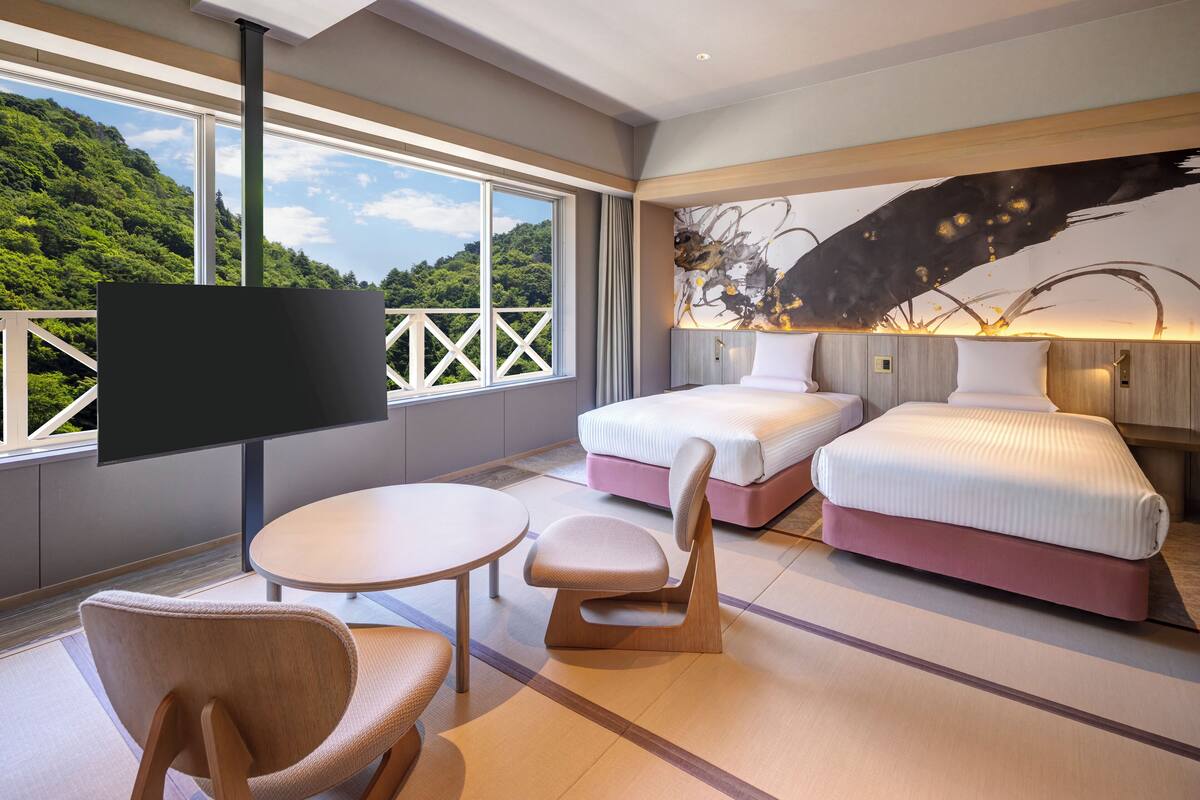A hotel room with a large window, two beds, a TV, a table, and a chair.