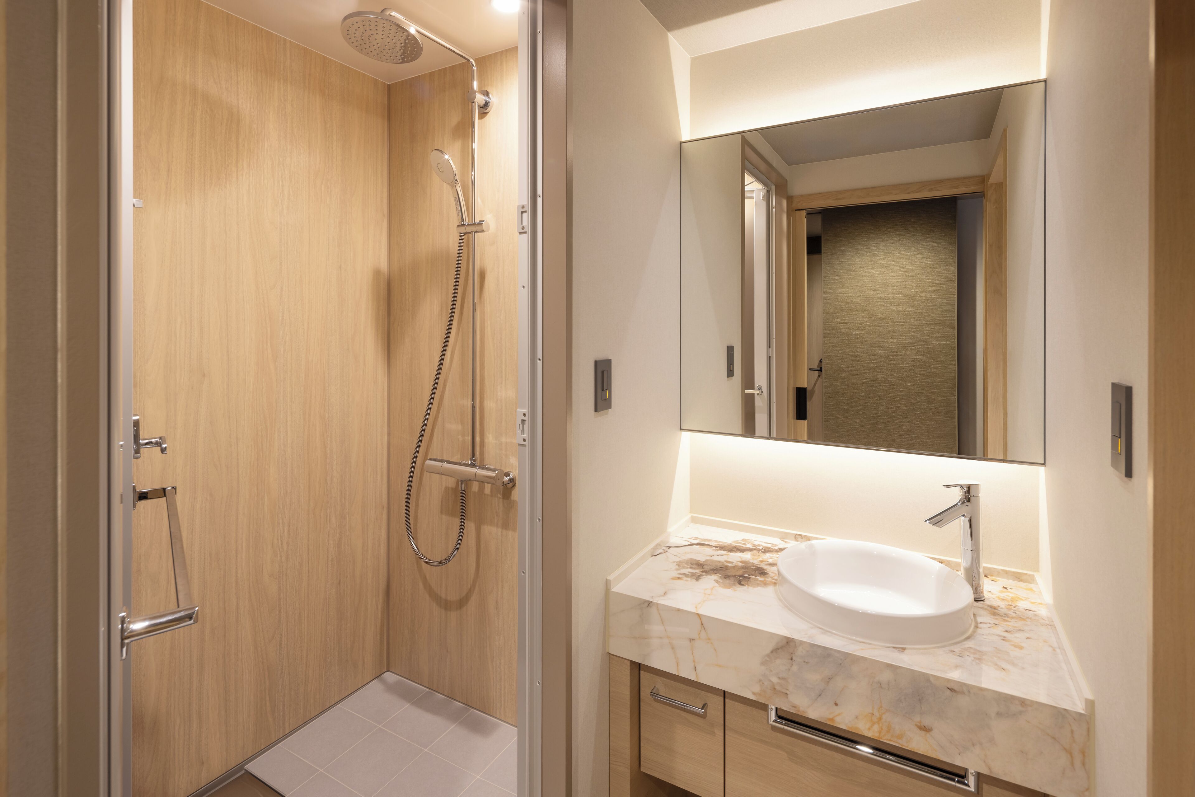 A modern bathroom with a wooden shower enclosure, a white sink with a marble countertop, and a large mirror above the sink.