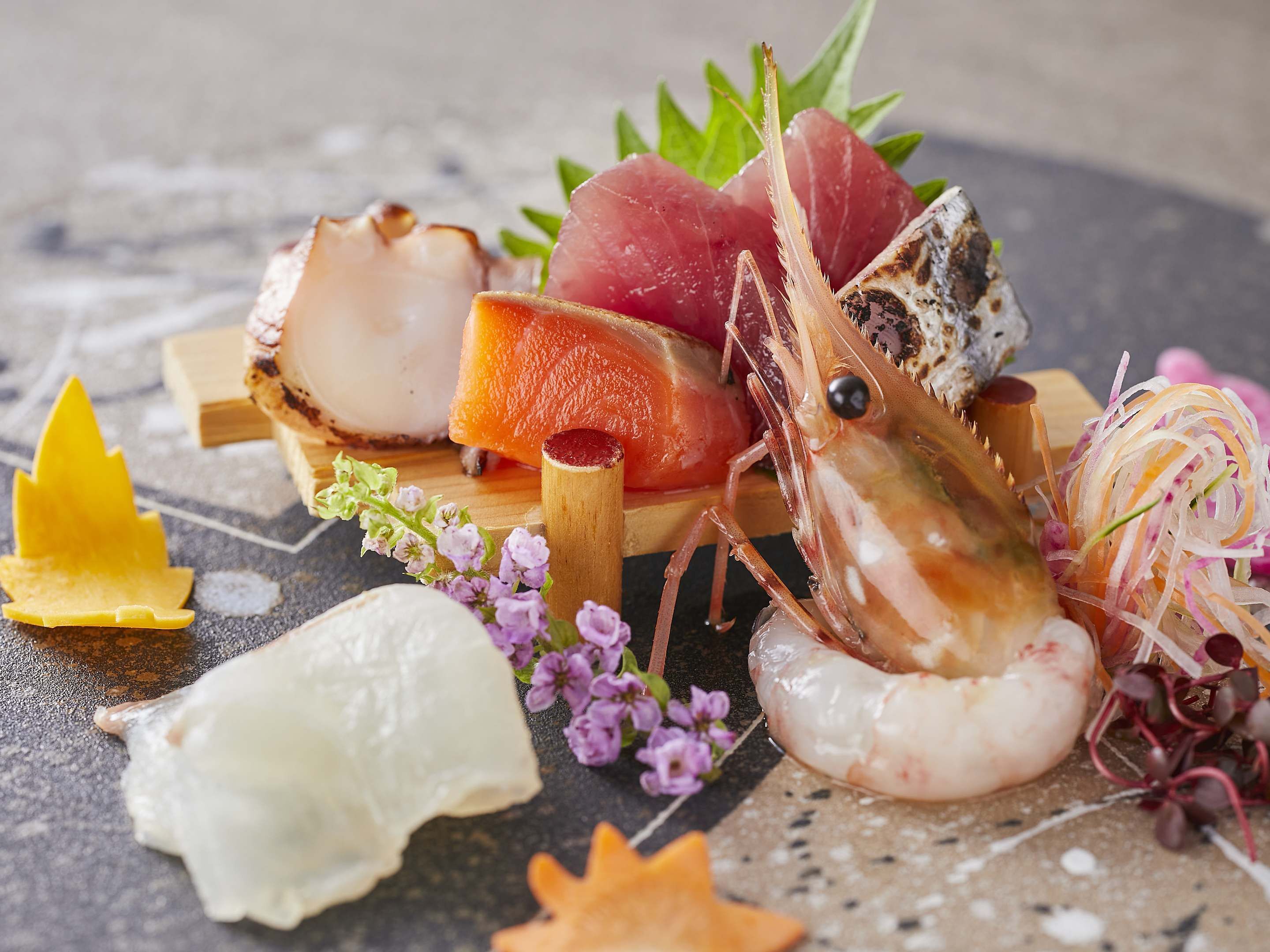 Une variété de fruits de mer, notamment des crevettes, des coquilles Saint-Jacques et des tranches de poisson, disposés sur une planche en bois agrémentée d’éléments décoratifs.