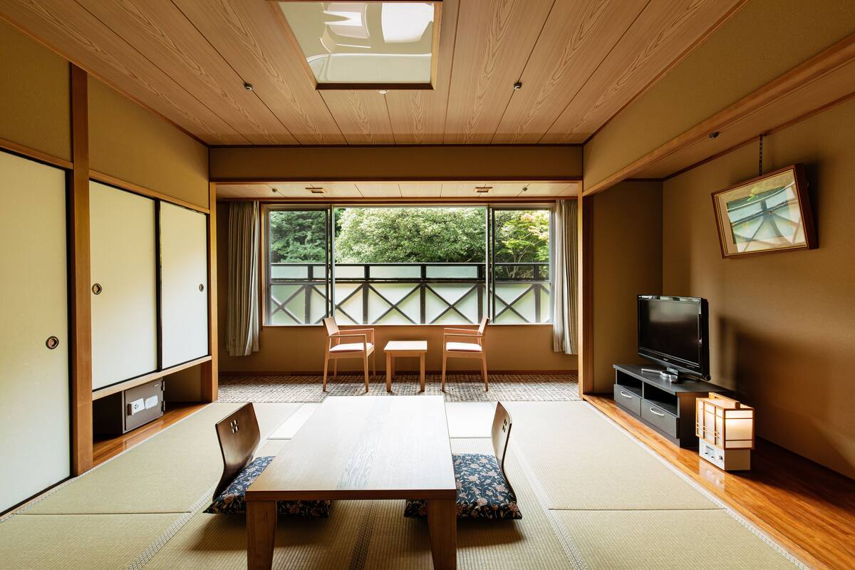 A traditional Japanese room with tatami flooring, a low table with cushions, a television, and a sliding door.